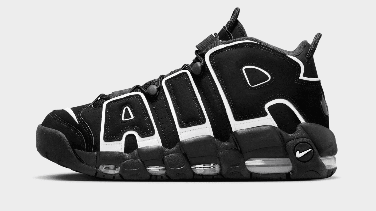 Nike Air More Uptempo colorway nero e bianco su sfondo neutro, vista laterale che evidenzia la scritta oversize sulla tomaia