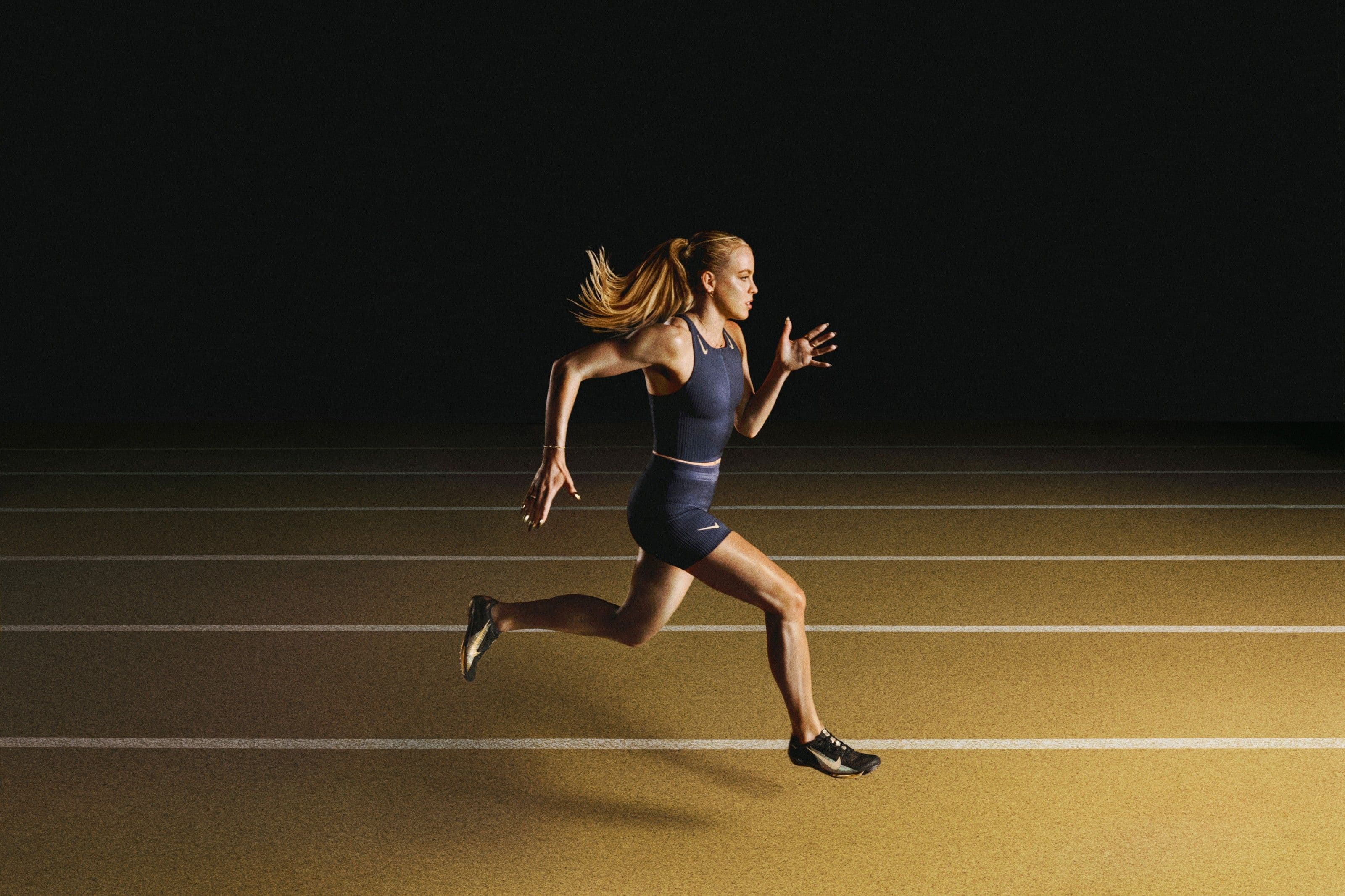 Scarpe da corsa in nero e oro della collezione running signature Keely Hodgkinson Nike su sfondo scuro con accenti metallici