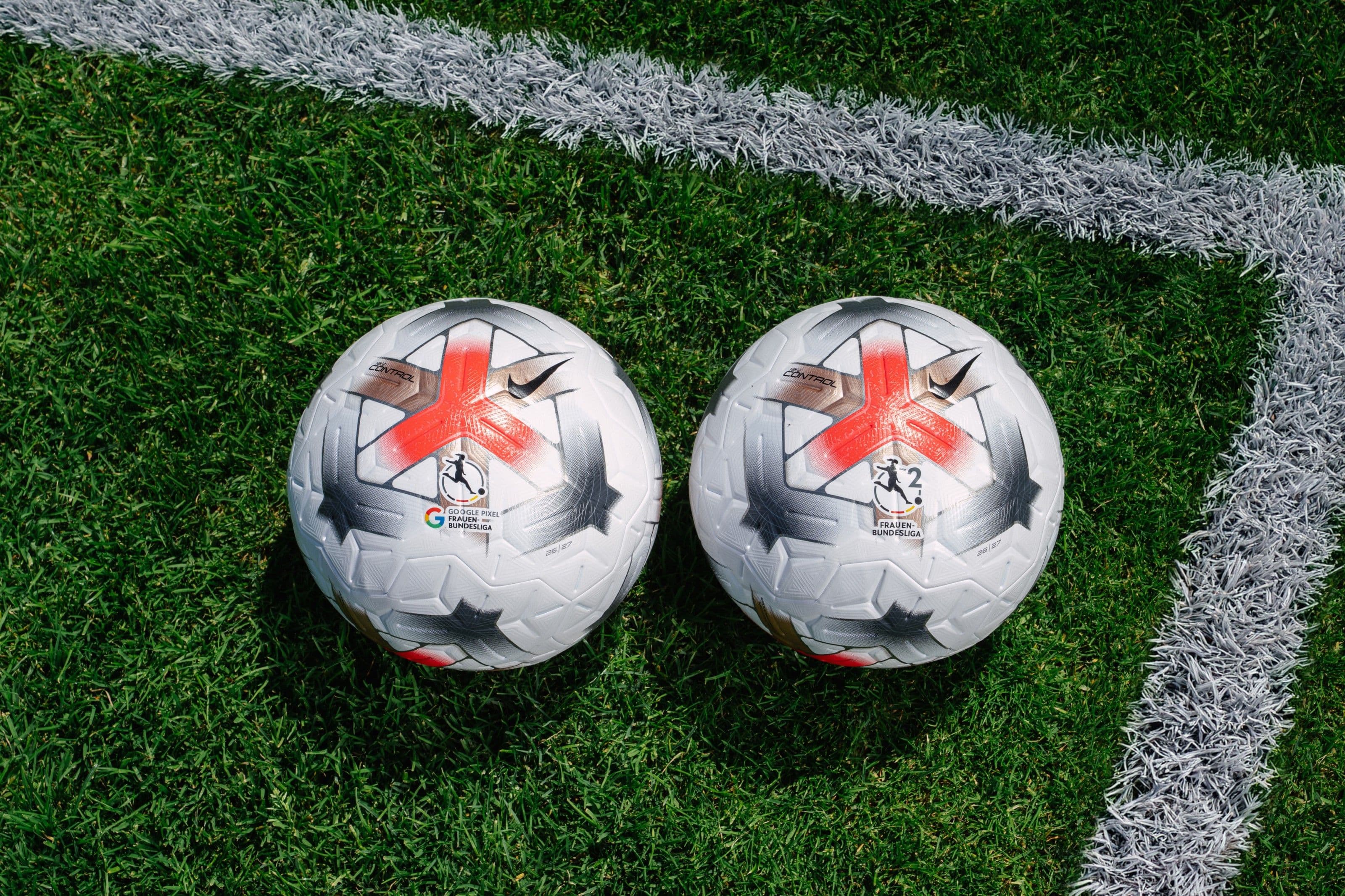 Pallone da calcio bianco con texture debossata su fondo scuro, luce laterale drammatica, dettaglio tecnico in stile editoriale sportivo